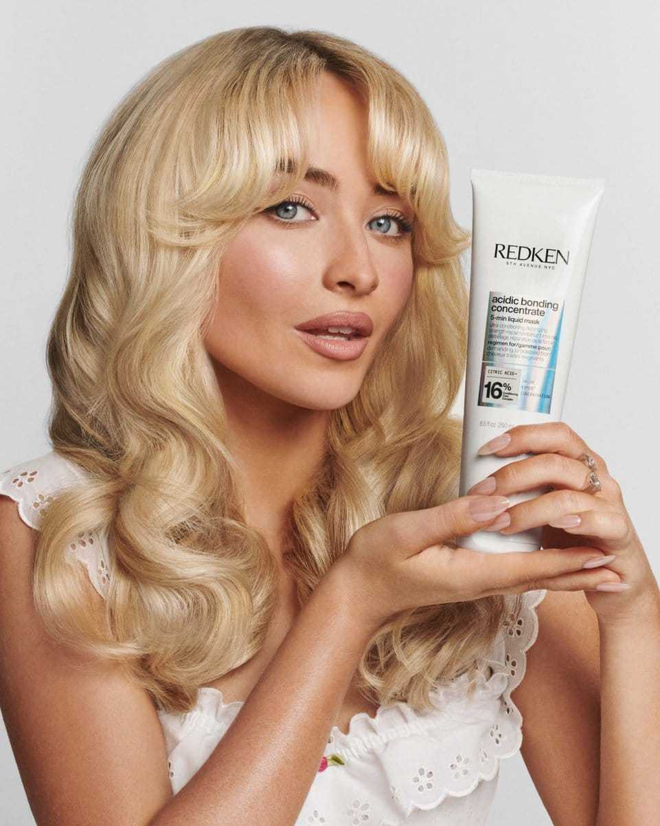 Blonde woman holding Redken hair care product, showcasing its packaging and features.