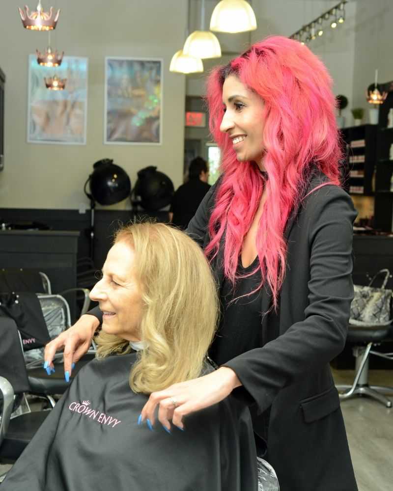 Stylist with bright pink hair styling a client's hair in a salon setting.