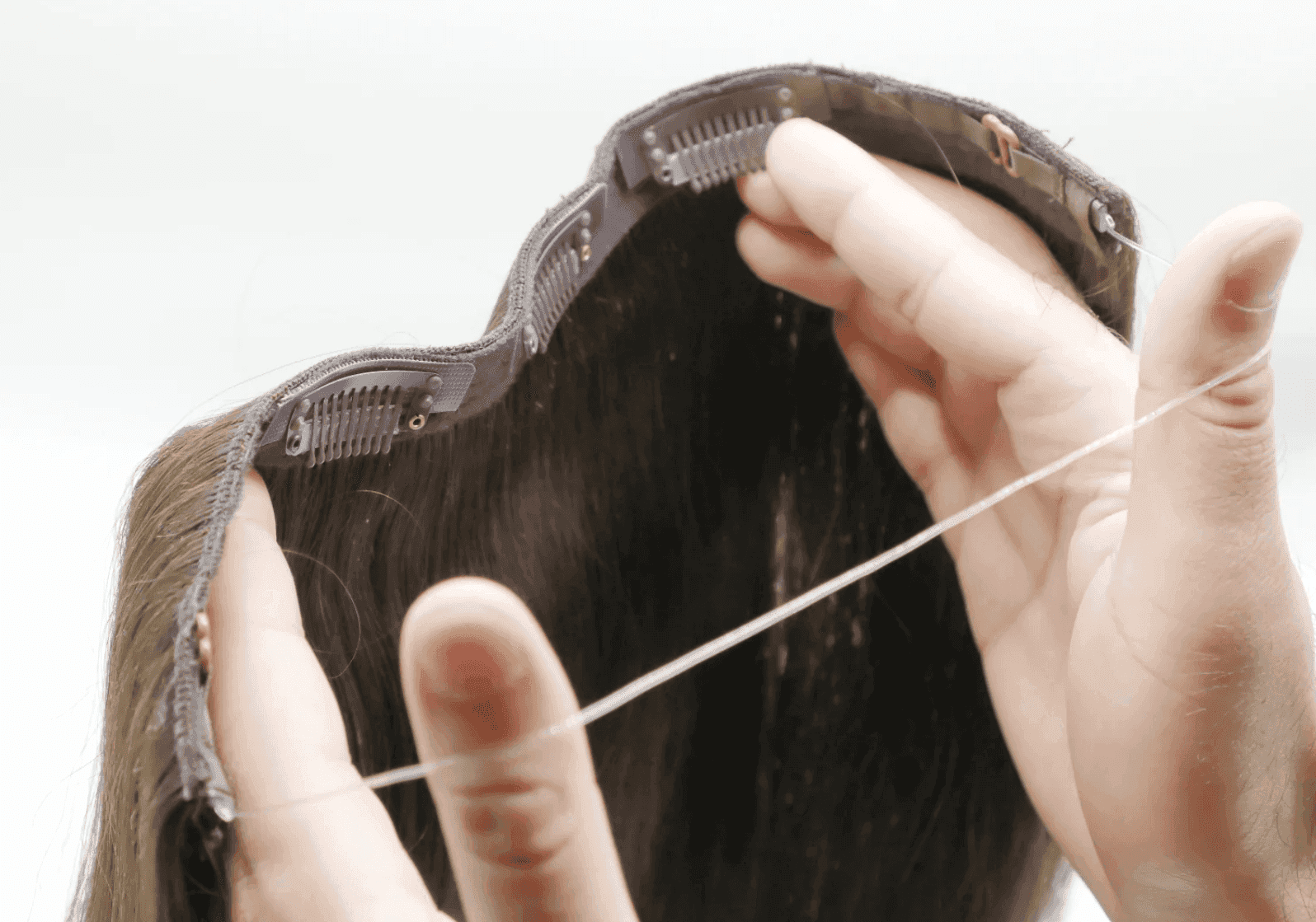 Hands holding brown clip-in hair extension against a white background.